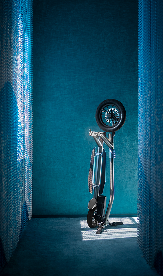 Black electric scooter against a blue wall with curtains